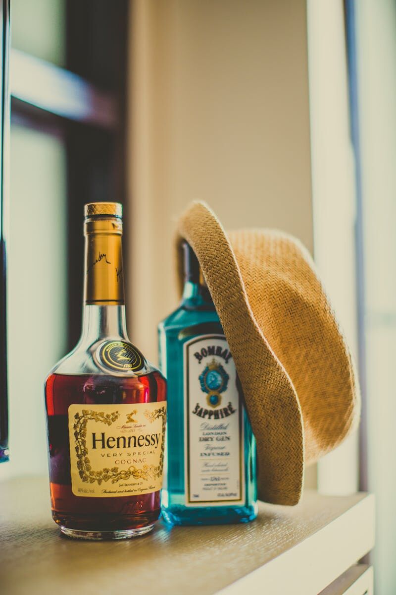 Stylish composition of Hennessy and Bombay Sapphire bottles with a straw hat.